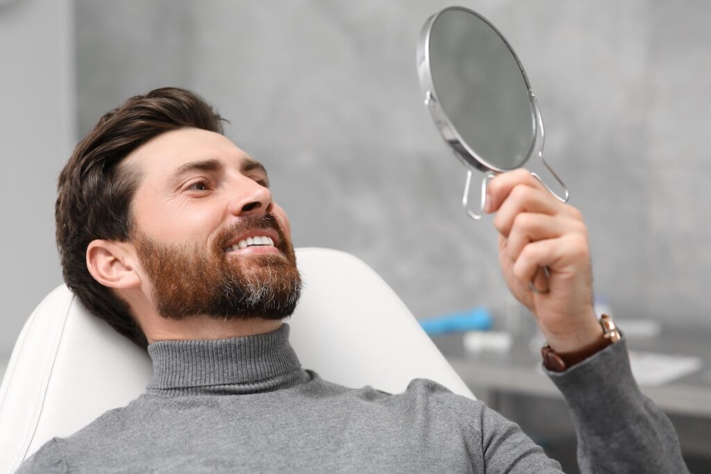 Man looking at his new dental implants in mirror indoors